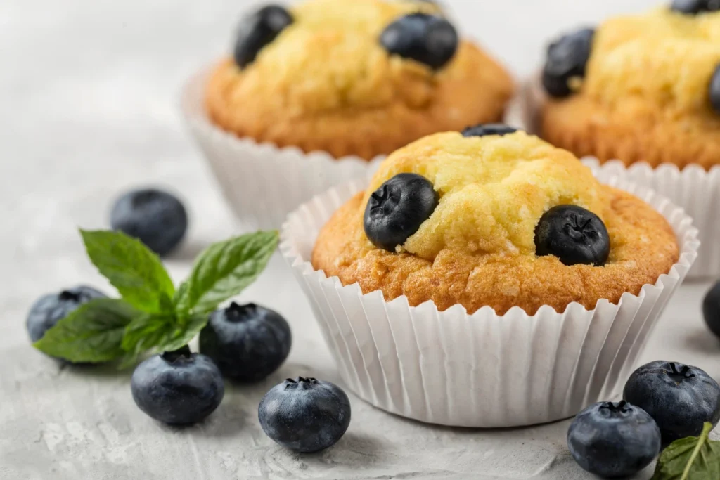 Blueberry muffin tops on a rustic table with a steaming cup of coffee beside them.