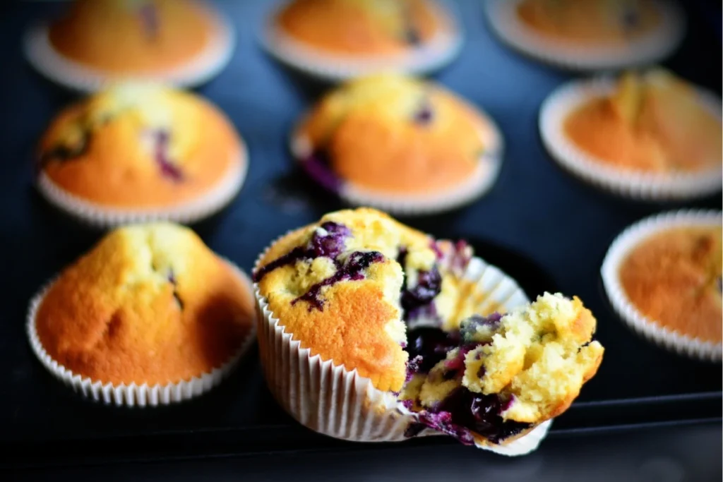 Rustic blueberry muffin tops with visible blueberries, dusted with sugar, on a wooden table."