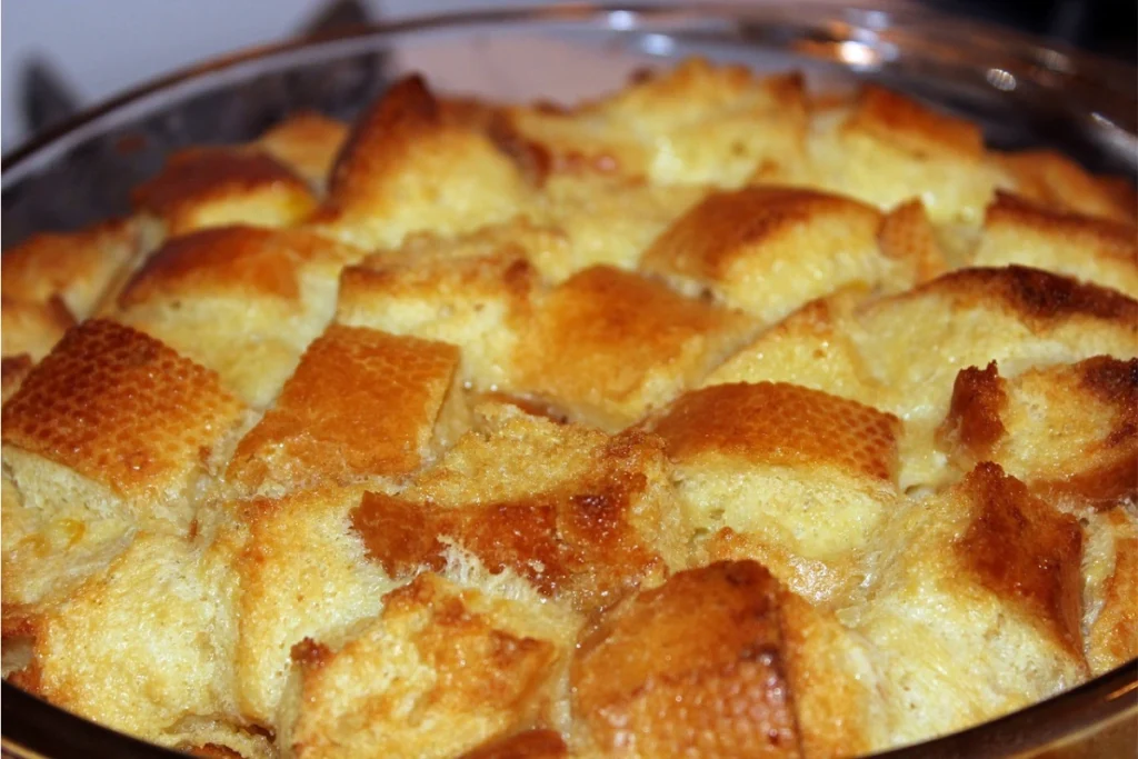 A loaf of caramel apple bread on a wooden board, with slices cut to reveal a moist interior, surrounded by apples and caramel sauce.