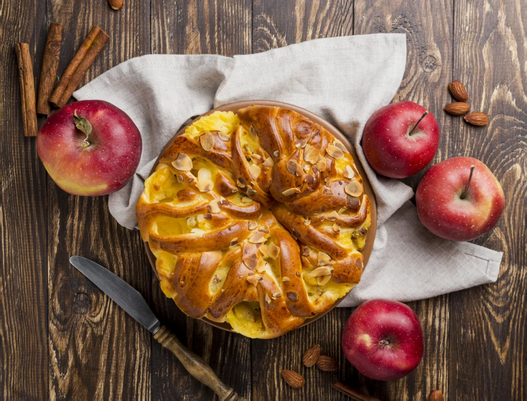 "Various versions of cinnamon roll apple pie with toppings like streusel, caramel sauce, and whipped cream, arranged on a rustic table."